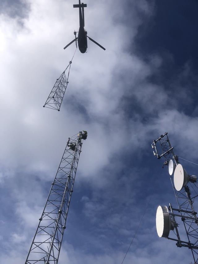 Helikopter løfter en mastseksjon mens klatrere står i masten